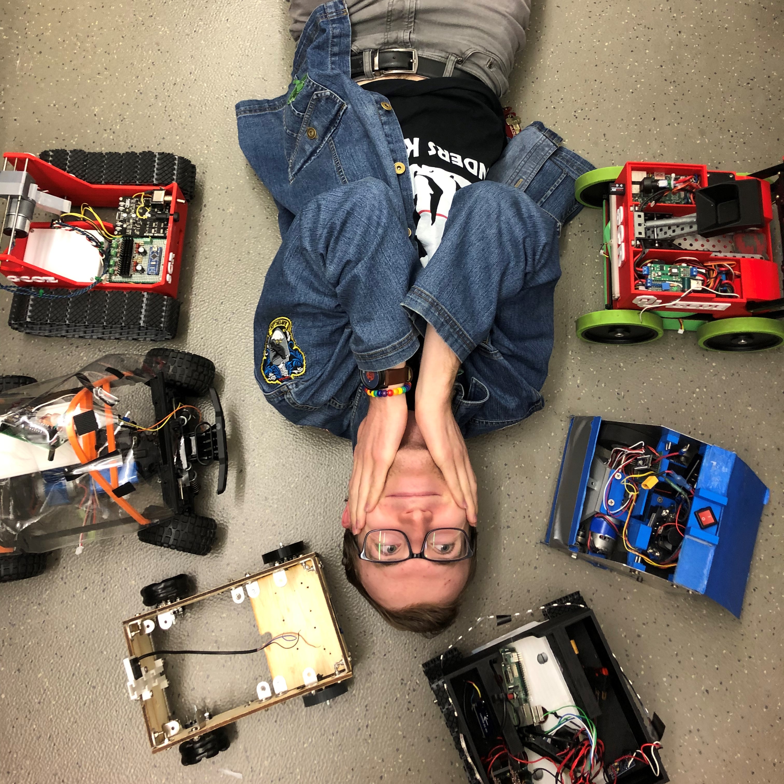Kevin laying on the lab floor surrounded by small robots